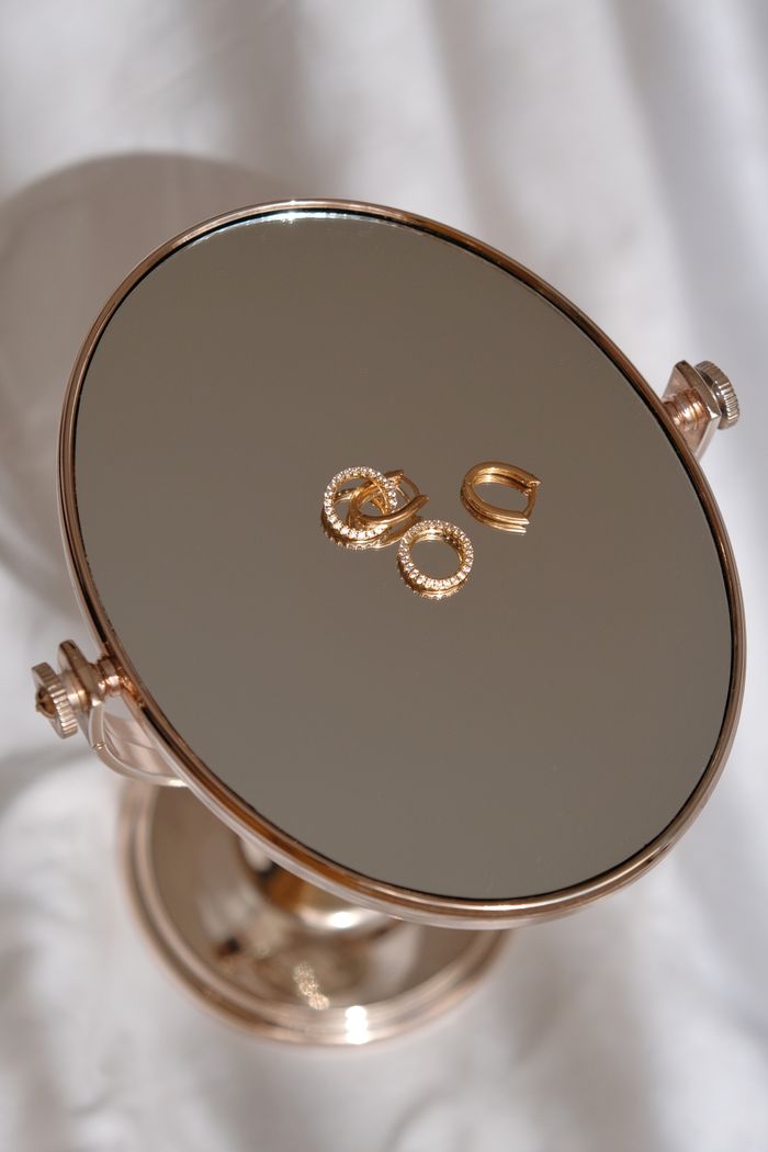 Elegant gold earrings showcased on a reflective round mirror, perfect for luxury accessory themes.