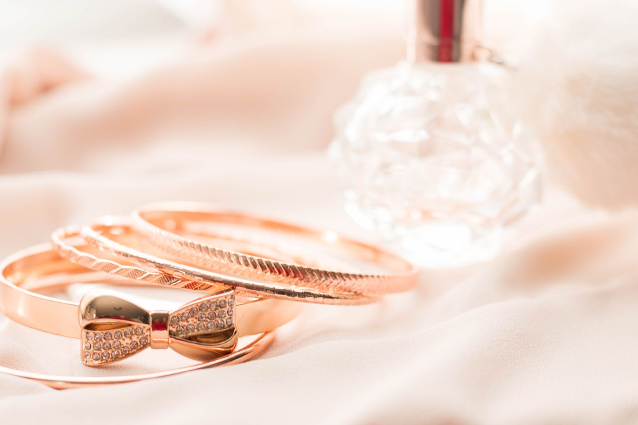 Luxurious gold bangles and crystal perfume bottle on silky pink fabric for a chic look.